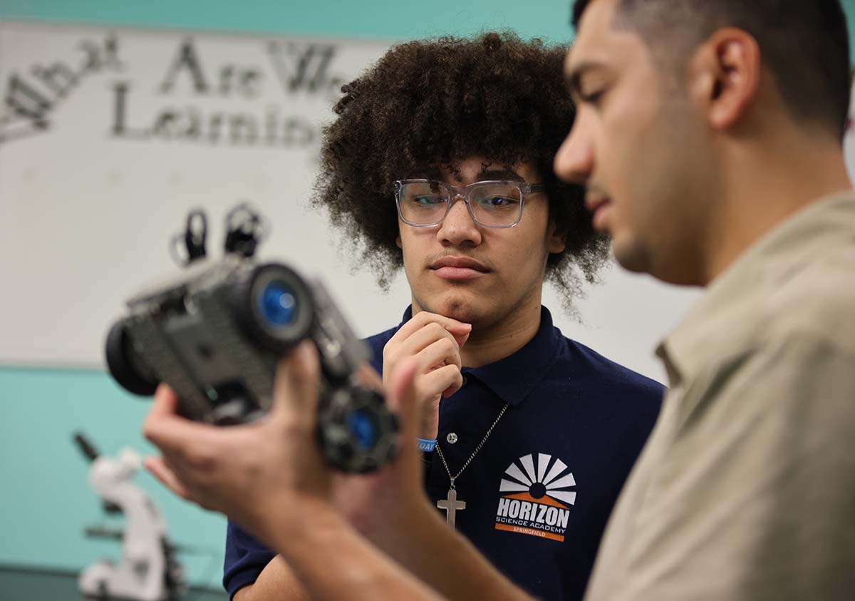 HSA Teacher smiles while kneeling beside a young student in a classroom setting.